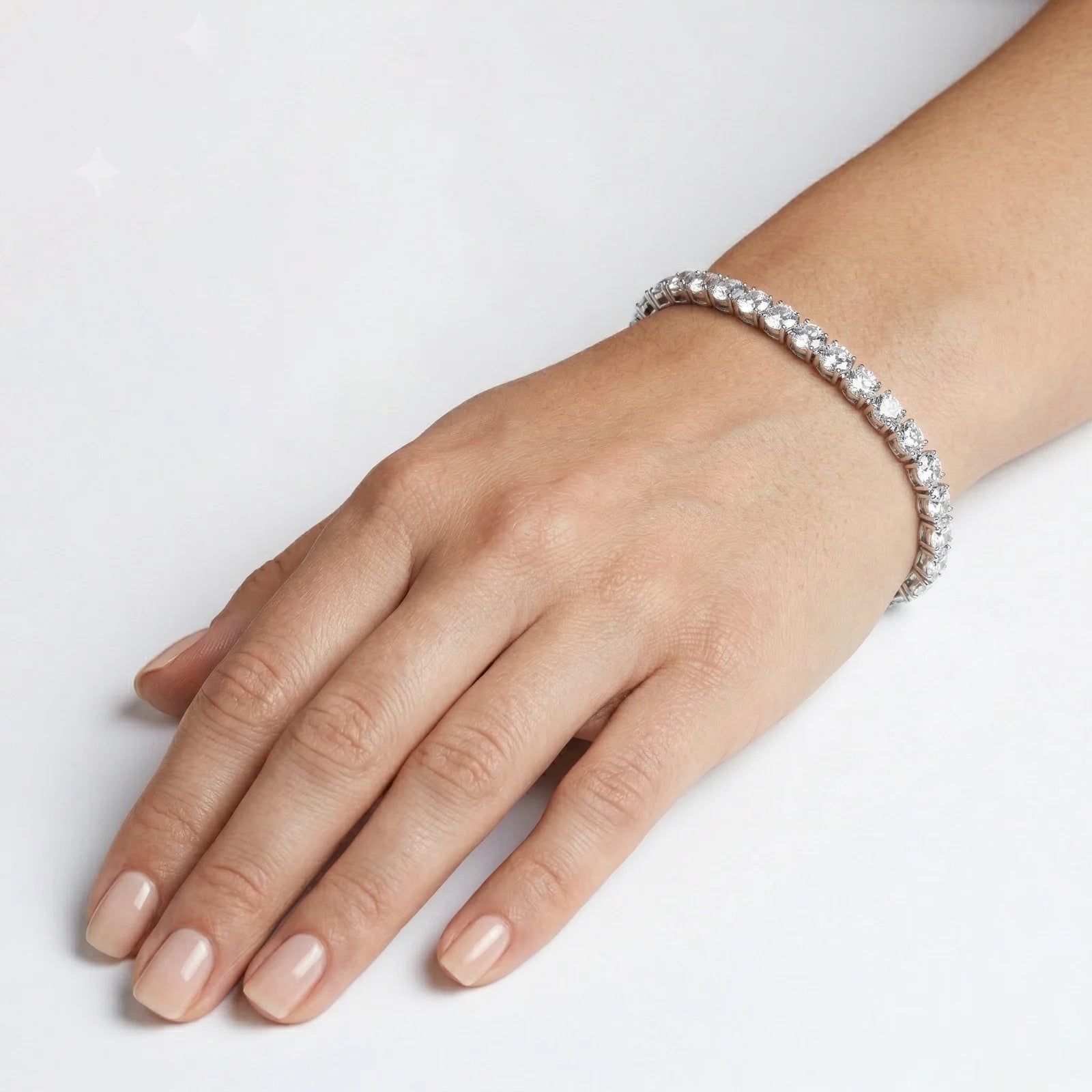 A close-up of a hand wearing a sparkling silver tennis bracelet on a clean white background.
