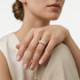 A close-up of a woman's hand wearing a delicate silver ring with three clear round-cut gemstones, set against a clean white background.