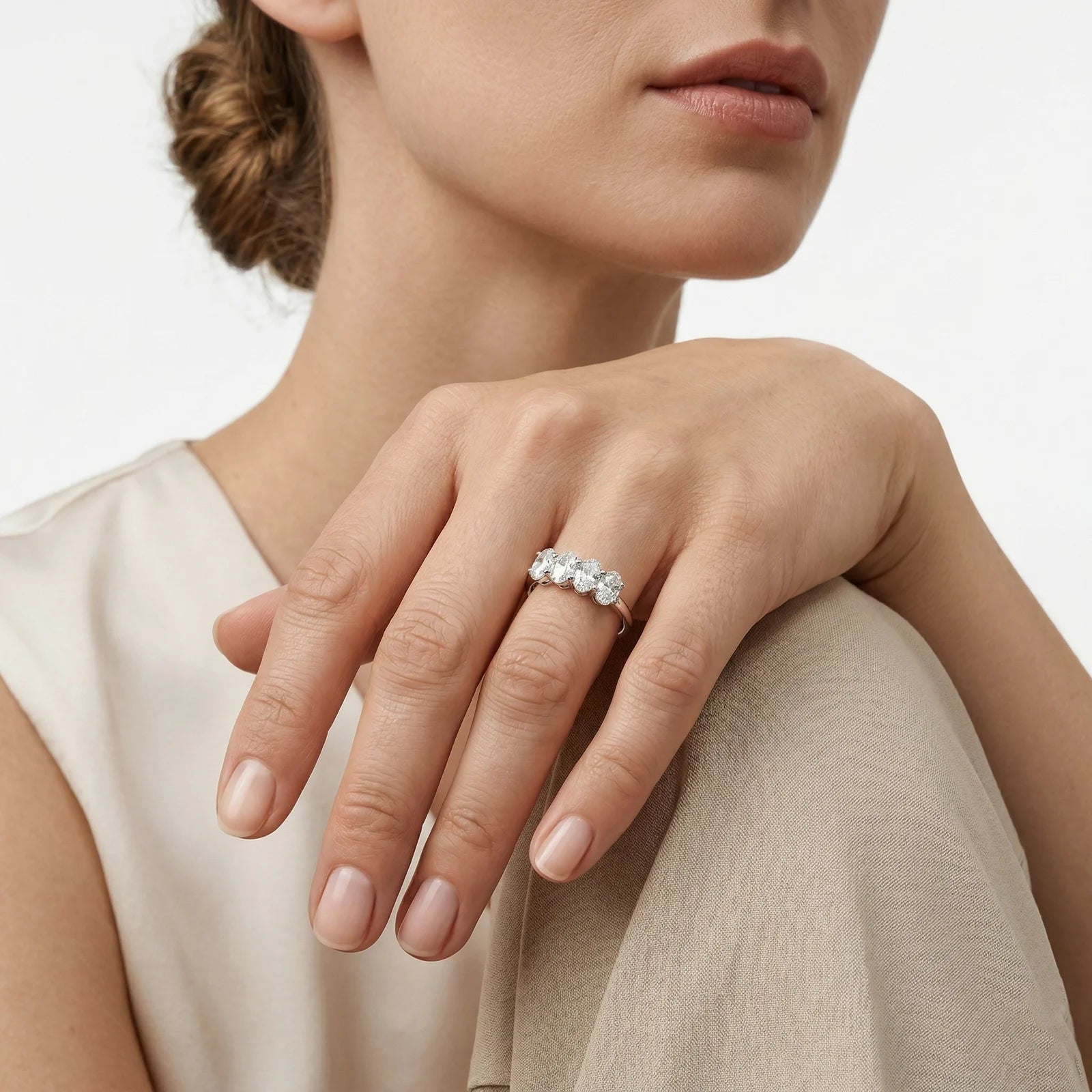 A close-up of a woman's hand wearing a delicate silver ring with three clear round-cut gemstones, set against a clean white background.