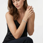 A woman wearing a delicate silver bracelet with clear stones, posed in a black satin top against a clean white background.
